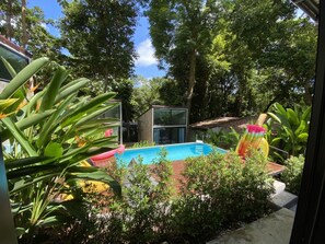 En trädgård med en pool, omgiven av frodig grönska och ett modernt hus.