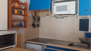 A compact kitchen with a microwave, stove, and sink. There are shelves with kitchenware and utensils. - Charming Studio in Verdant Setting with Balcony, Sleeps 4 (Le Biot)