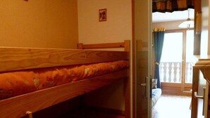 A bunk bed room with a wooden headboard, a small window with curtains, and a balcony visible through an open door. - Charming Studio in Verdant Setting with Balcony, Sleeps 4 (Le Biot)