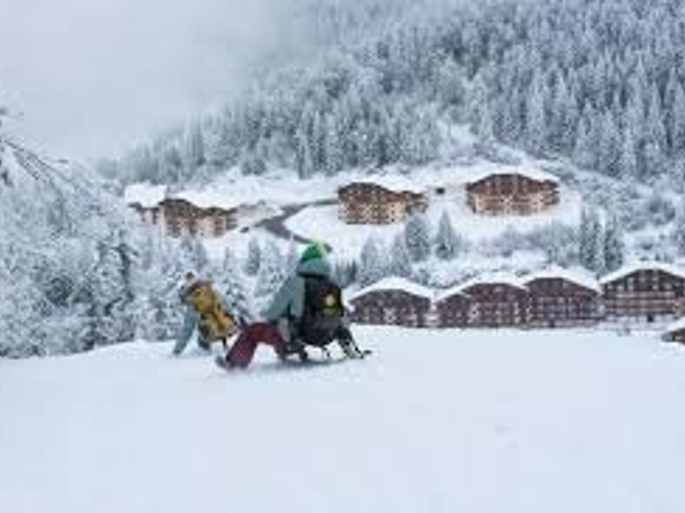 Ein schneegebdeckter Berg mit einer Skipiste und Gebäuden im Hintergrund.