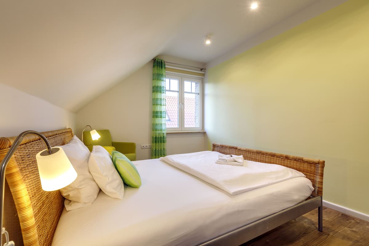 Een net opgemaakt bed met witte lakens, een groen kussen en een lamp aan de linkerkant.