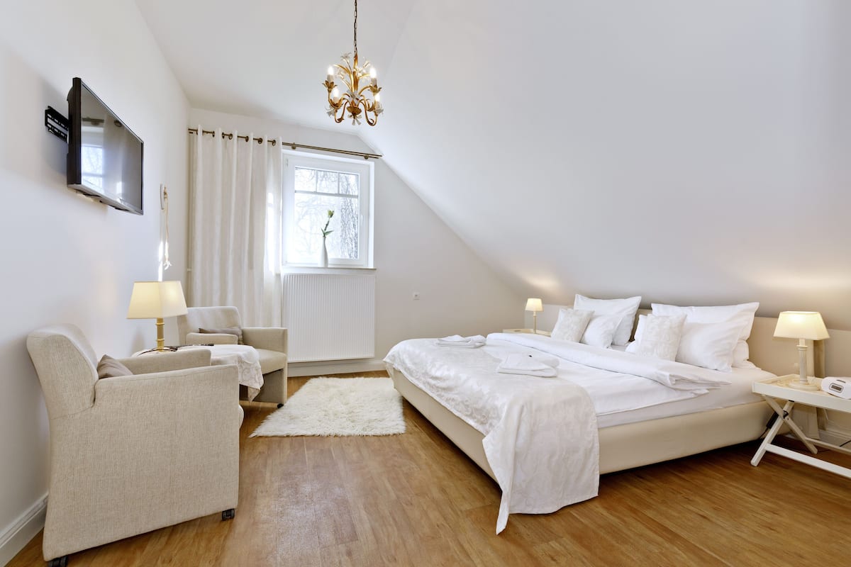 Een moderne slaapkamer met een groot bed, twee nachtkastjes met lampen, een aan de muur bevestigde televisie en een raam met gordijnen.