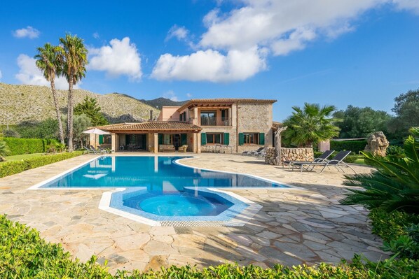A house with a swimming pool, stone patio, and a mountain in the background.