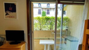 A room with a sliding glass door leading to a balcony, a small white table, and a wooden cabinet with a television.