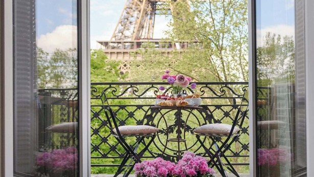 A balcony with a view of the Eiffel Tower, a table with flowers, and a railing. - Enjoy Eiffel Tower Sparkle in Grand Style! (Paris)