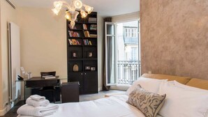 A hotel room with a bed, a desk, a bookshelf, and a view of the outside. - Enjoy Eiffel Tower Sparkle in Grand Style! (Paris)