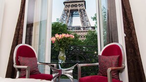 A room with a view of the Eiffel Tower through a window. There are two red upholstered chairs and a small table with a vase of flowers. - Enjoy Eiffel Tower Sparkle in Grand Style! (Paris)