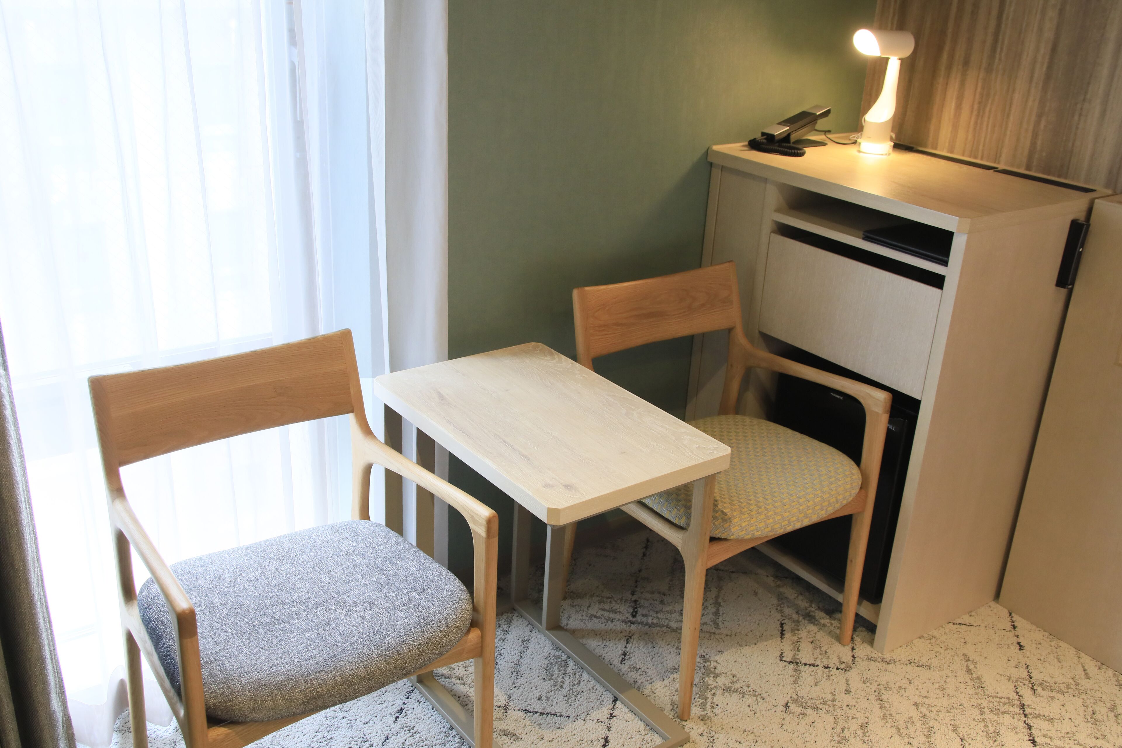A small room with a wooden table and two chairs, a desk with a lamp, and a cabinet.