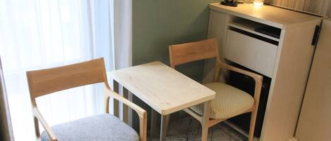 A small room with a wooden table and two chairs, a desk with a lamp, and a cabinet.