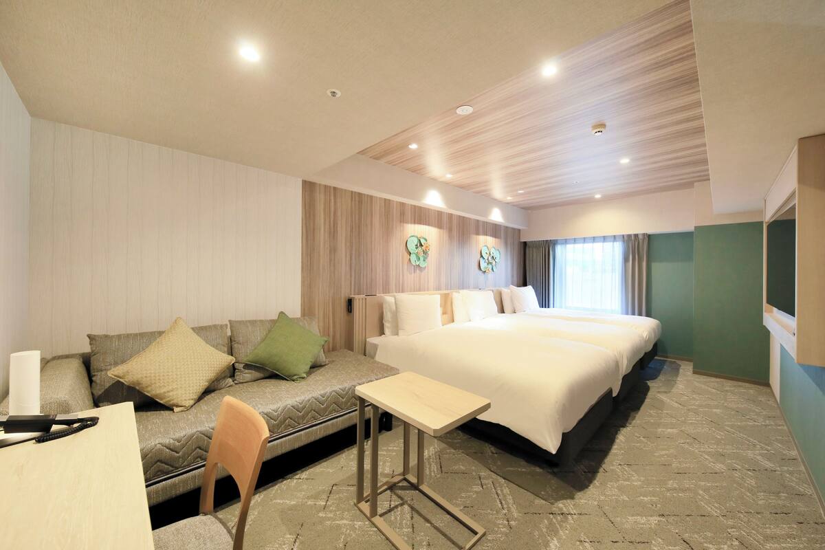 A hotel room with a bed, a sofa, a small table, and a desk with a chair.