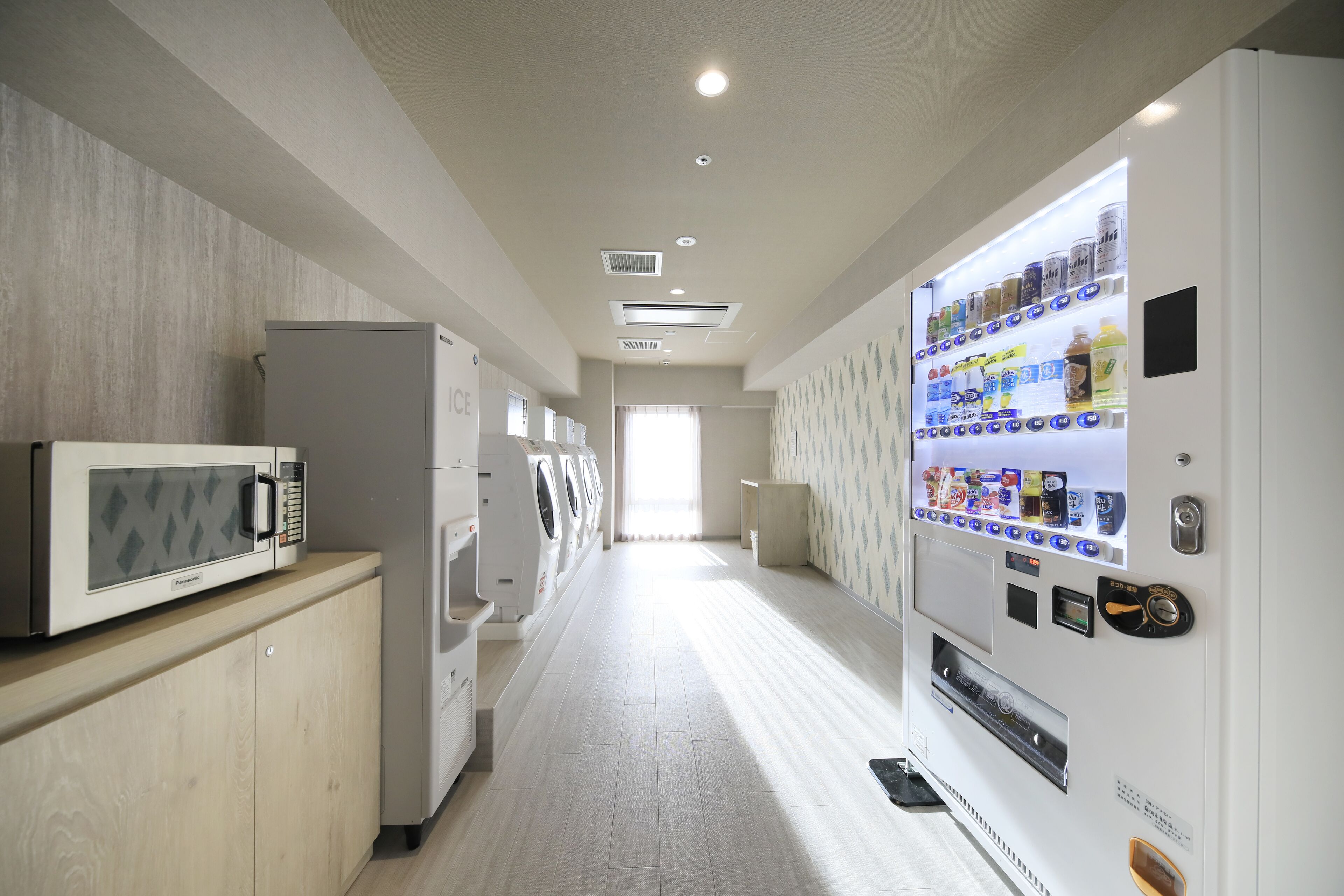 A hotel corridor with a microwave, washing machines, and a vending machine.