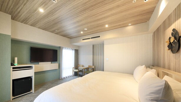 Una habitación de hotel moderna con una cama grande, un televisor de pantalla plana montado en la pared, un escritorio con una computadora y una pequeña zona de estar con una mesa y sillas.