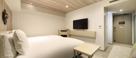 Hotelkamer met een groot bed, een kleine tafel, een aan de muur bevestigde televisie en een deur naar een andere kamer.