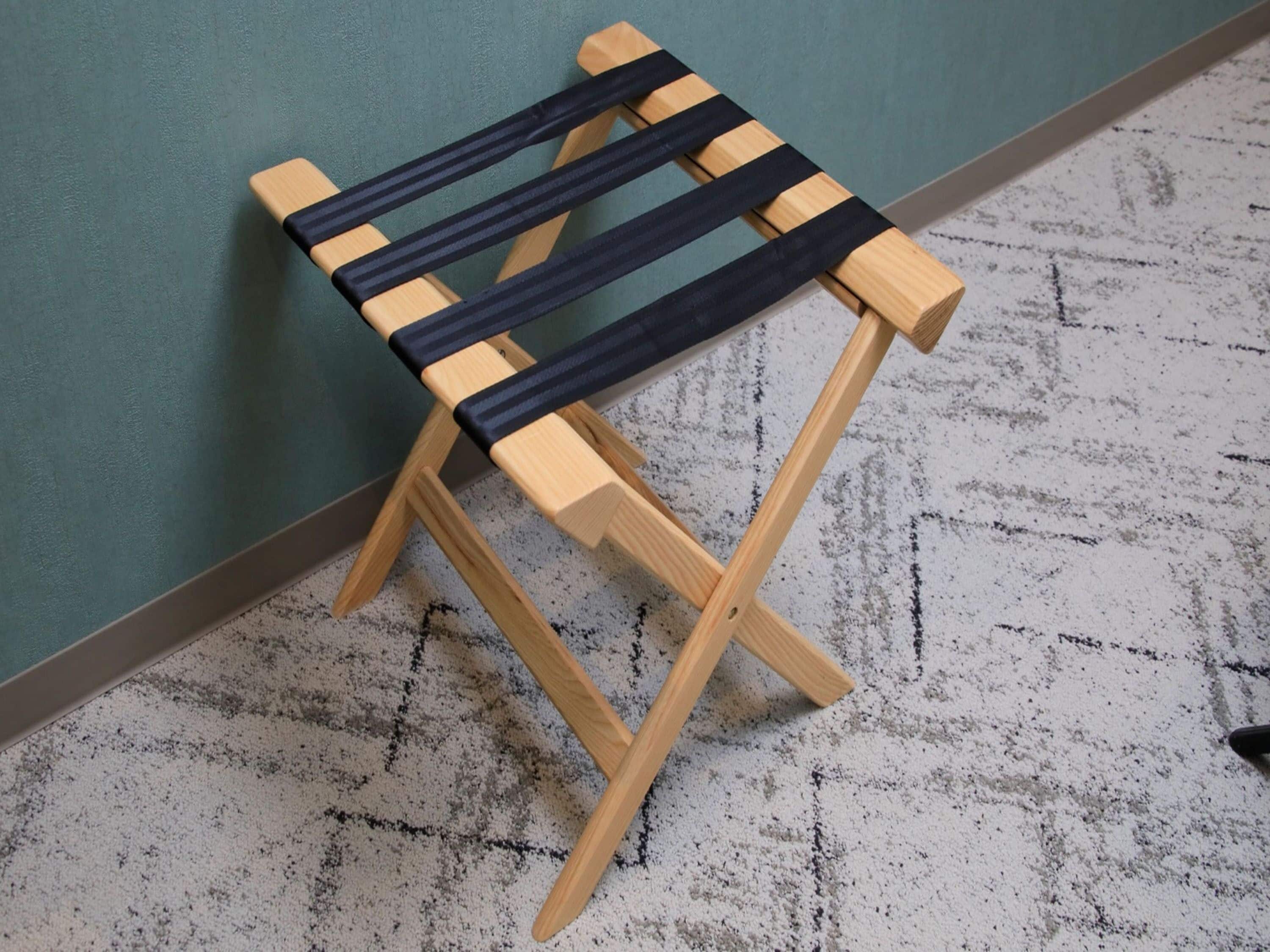 A small wooden stool with black straps, positioned against a teal wall and a speckled floor.