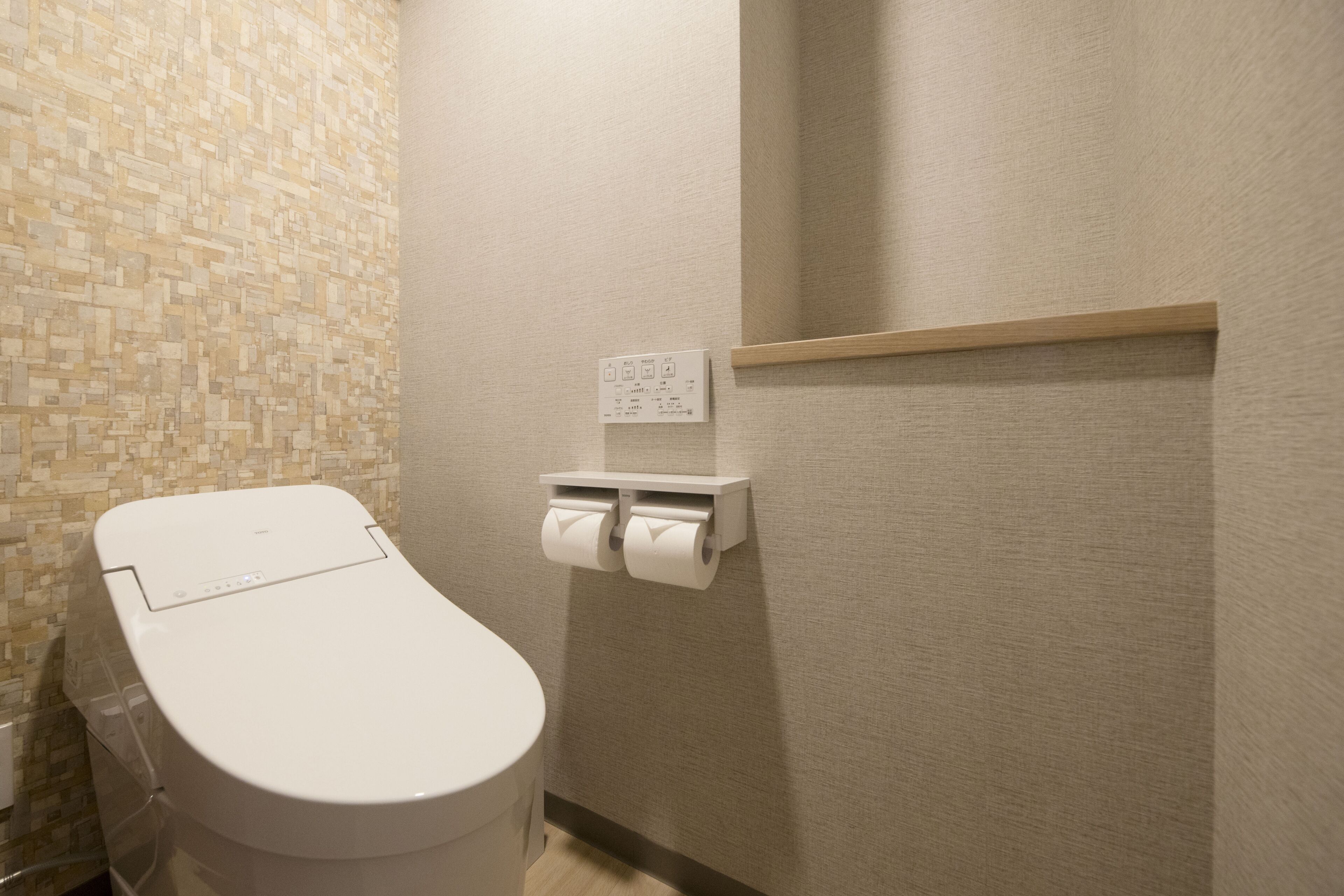 A bathroom with a toilet, a wall-mounted paper towel dispenser, and a small shelf.