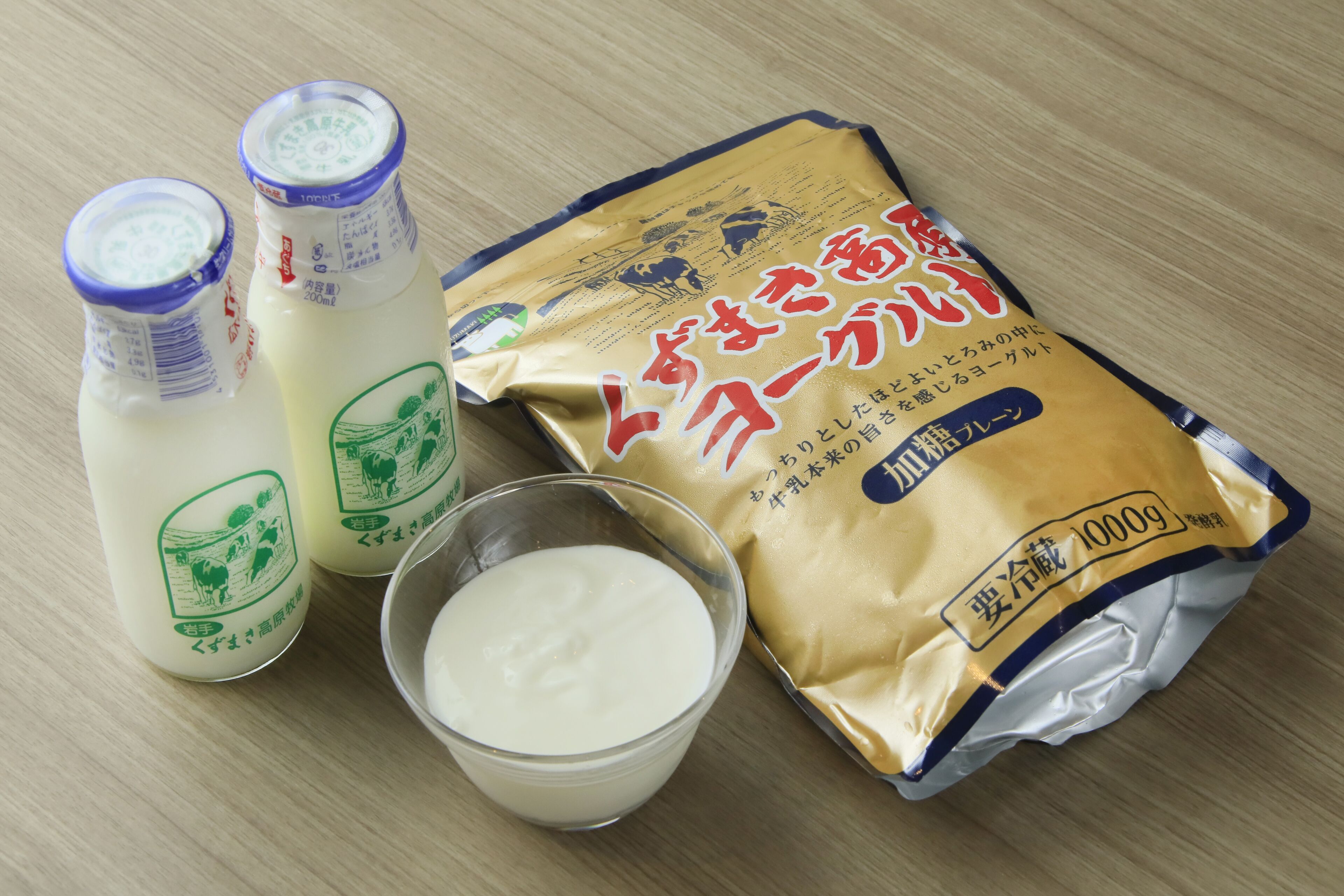 Two bottles of milk, a bowl of milk, and a packet of milk powder on a wooden surface.