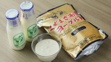 Two bottles of milk, a bowl of milk, and a packet of milk powder on a wooden surface.