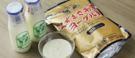 Two bottles of milk, a bowl of milk, and a packet of milk powder on a wooden surface.