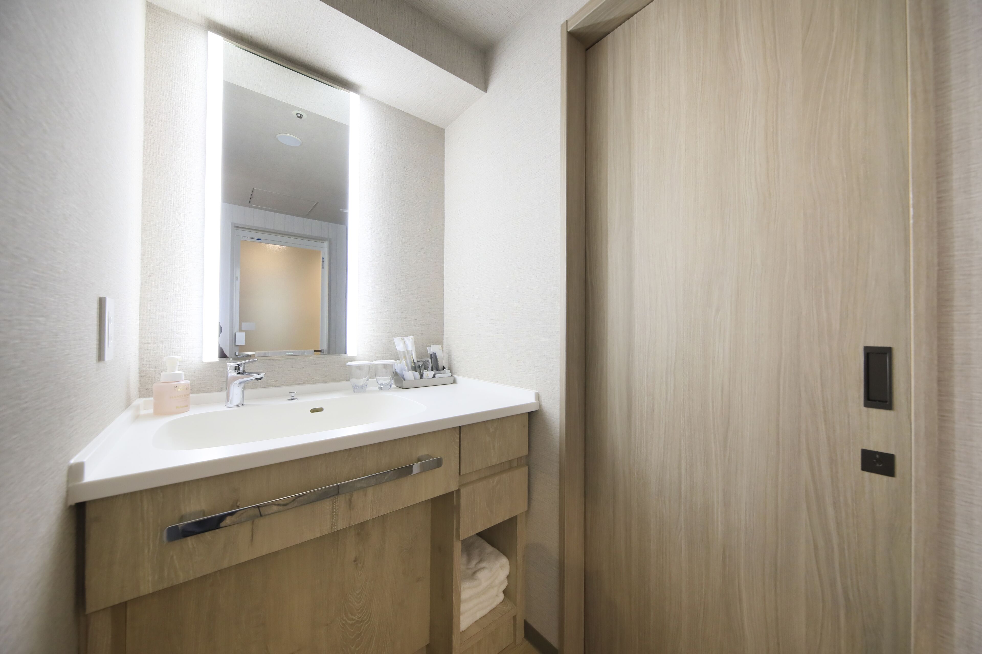 A modern bathroom with a white sink, mirror, and wooden vanity.