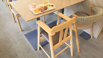 A dining area with a wooden table and chairs, a tray with food and drinks, and a patterned cushion on one chair.