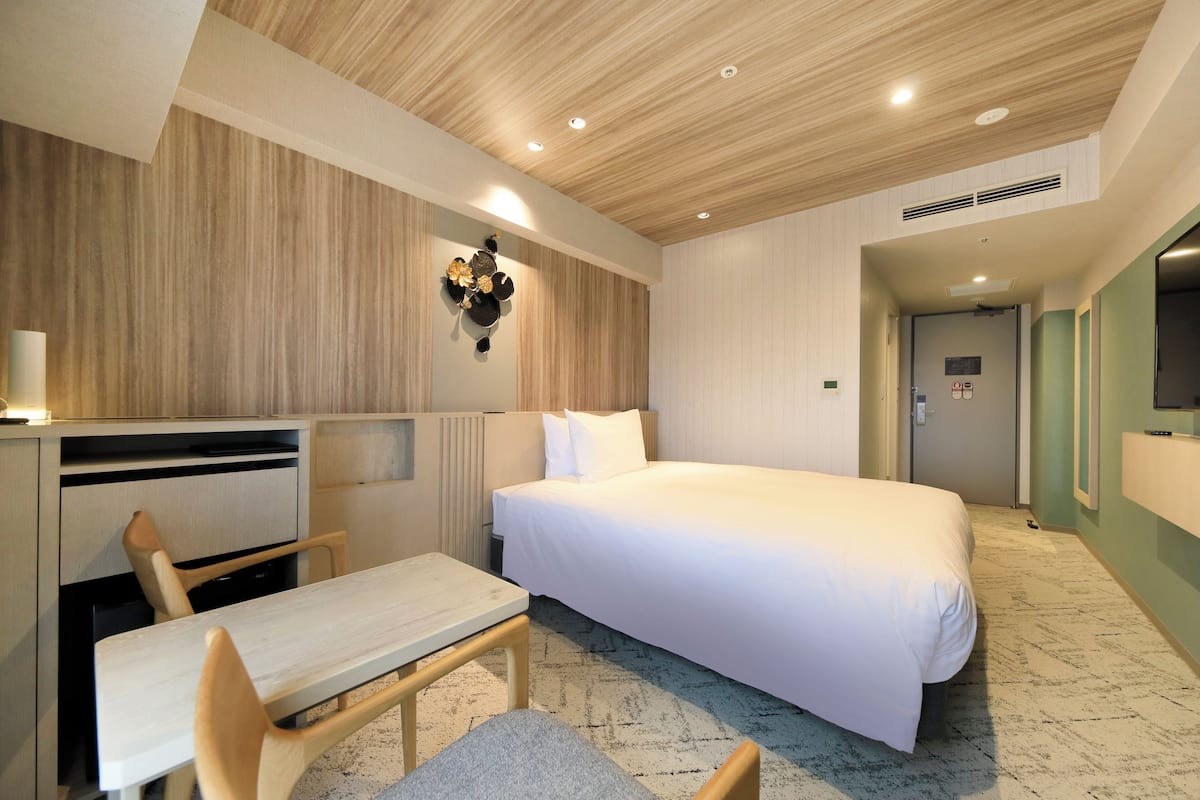 A hotel room with a bed, desk, chair, and a wall-mounted decorative item.