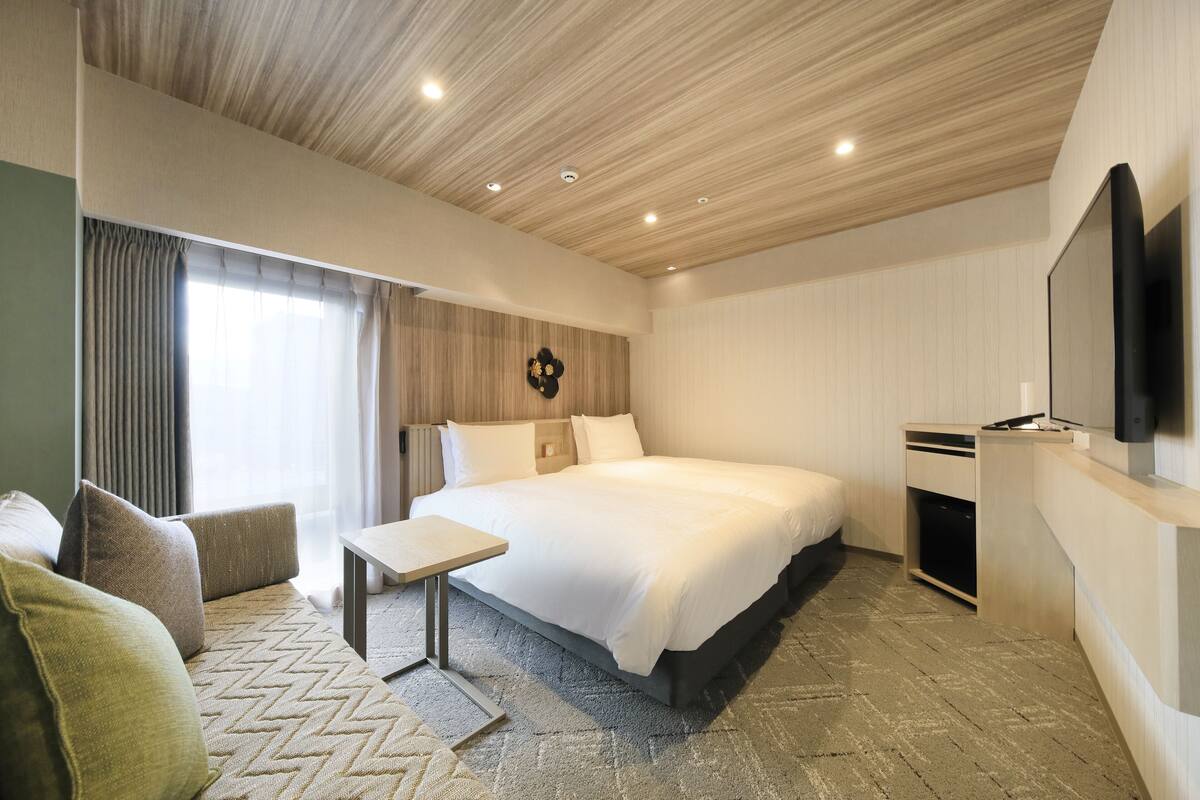A modern hotel room with a large bed, a bedside table, a flat-screen TV mounted on the wall, and a small desk with a chair.
