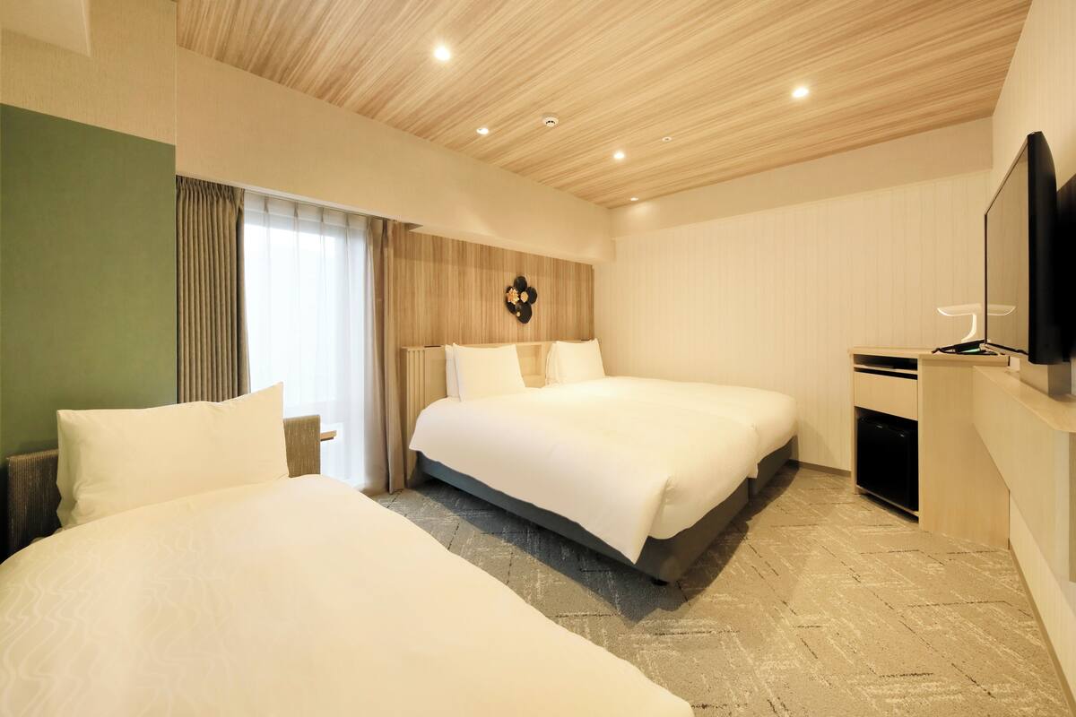 A hotel room with two beds, a television, a desk, and a window with curtains.