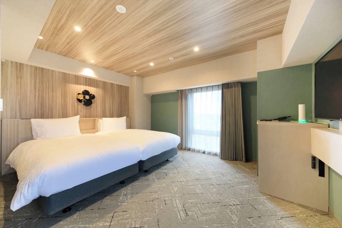 A modern bedroom with a large bed, a wooden ceiling, a green accent wall, and a desk with a lamp.