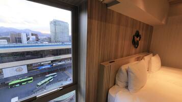 A hotel room with a bed, a window with a view of a cityscape, and a wooden headboard.