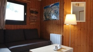 Um quarto aconchegante com parede de madeira, um sofá, uma mesa com xícaras, um abajur e uma pintura de uma montanha.