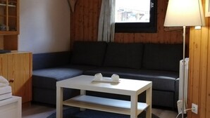 Quarto aconchegante com um sofá azul escuro, uma mesa de centro branca, um abajur e uma janela com cortina.