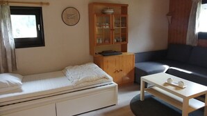 Um quarto pequeno e aconchegante com uma cama de solteiro, um armário de madeira com portas de vidro, um sofá e uma mesa pequena.
