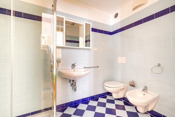 A bathroom with a glass shower enclosure, a sink, a toilet, and a bidet.