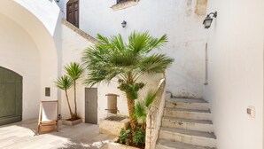 A courtyard with a staircase, a wooden chair, and potted plants. - Antica Dimora Stasi by BarbarHouse (Acquarica del Capo)