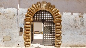 An arched stone doorway with a metal gate, leading into a courtyard with a bench and potted plants. - Antica Dimora Stasi by BarbarHouse (Acquarica del Capo)