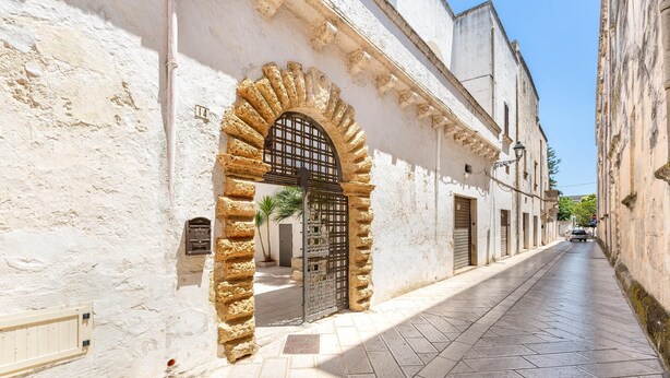 A narrow street with a stone archway leading to a building with a metal gate. - Antica Dimora Stasi by BarbarHouse (Acquarica del Capo)