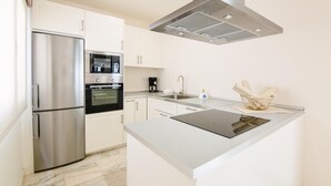 A modern kitchen with stainless steel appliances, a built-in oven, a coffee maker, and a small island with a sink. - Royal Villa 2 people Alegria (La Oliva)