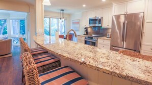Una cocina moderna con encimeras de granito, electrodomésticos de acero inoxidable y una isla grande con taburetes de bar.