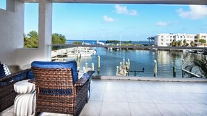 A balcony with wicker furniture overlooking a marina with boats and buildings in the background.