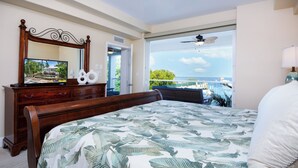 A bedroom with a large bed, a wooden dresser, a mirror, and a view of the ocean.
