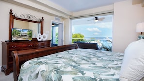 A bedroom with a large bed, a wooden dresser, a mirror, and a view of the ocean.