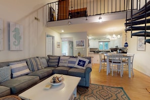 Relax in this open-plan living space featuring a cozy seating area and kitchen with white cabinetry.