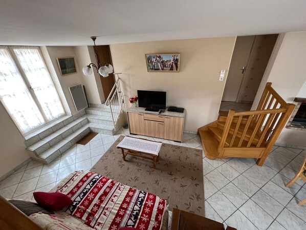A living room with a sofa, a wooden chair, a TV on a wooden cabinet, a staircase, and a painting on the wall. - Spacious Split-Level Cottage with Terrace near Saint-Dié - Sleeps 5 (Taintrux)