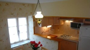 A small kitchen with a dining table, chairs, a vase with flowers, a hanging light fixture, and a microwave.