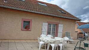 A patio with a table and chairs, a barbecue grill, and a building with a tiled roof and windows.