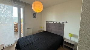 A bedroom with a large bed, a nightstand, a lamp, a radiator, and a window with blinds. - 2-Bedroom Cabin Apartment with Parking, Lake View (Les Angles)