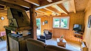 Ein gemütliches Blockhaus mit Kamin aus Stein, einem Fernseher und einer komfortablen Sitzecke.