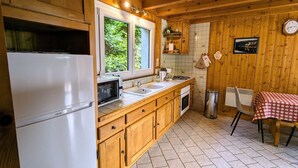Eine kleine Küche mit Holzausstattung, einem weißen Kühlschrank, einer Mikrowelle, einem Spülbecken und einem Essbereich mit Tisch und Stühlen.