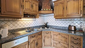 A kitchen with wooden cabinets, a granite countertop, a built-in oven, and a coffee maker. - Charming Mountain View Cottage Near Gérardmer: Spacious, Cozy, Garden, Parking, Ideal for Hikes (Jussarupt)