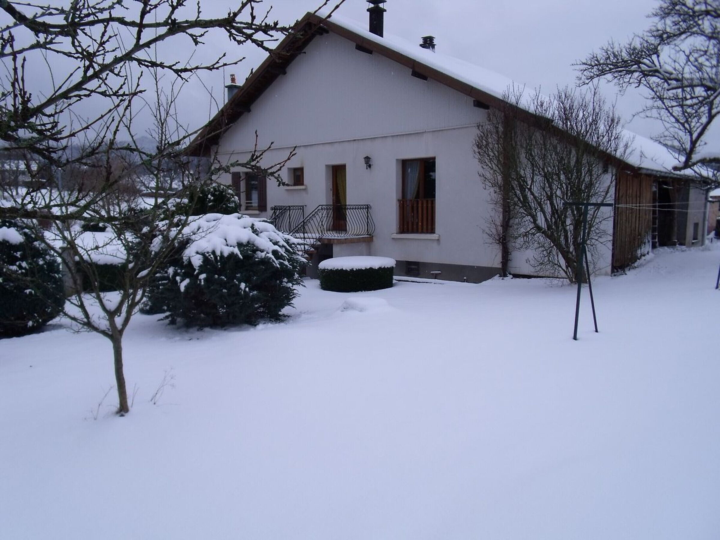 Une maison recouverte de neige, dotée d’un balcon en bois, d’un petit jardin et d’une pelouse enneigée.